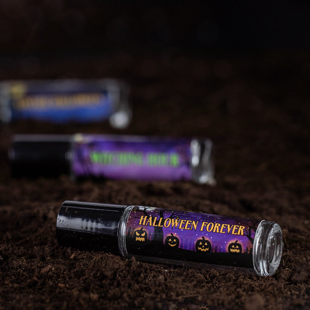 three perfume oil roll ons on dirt. halloween forever label is in focus