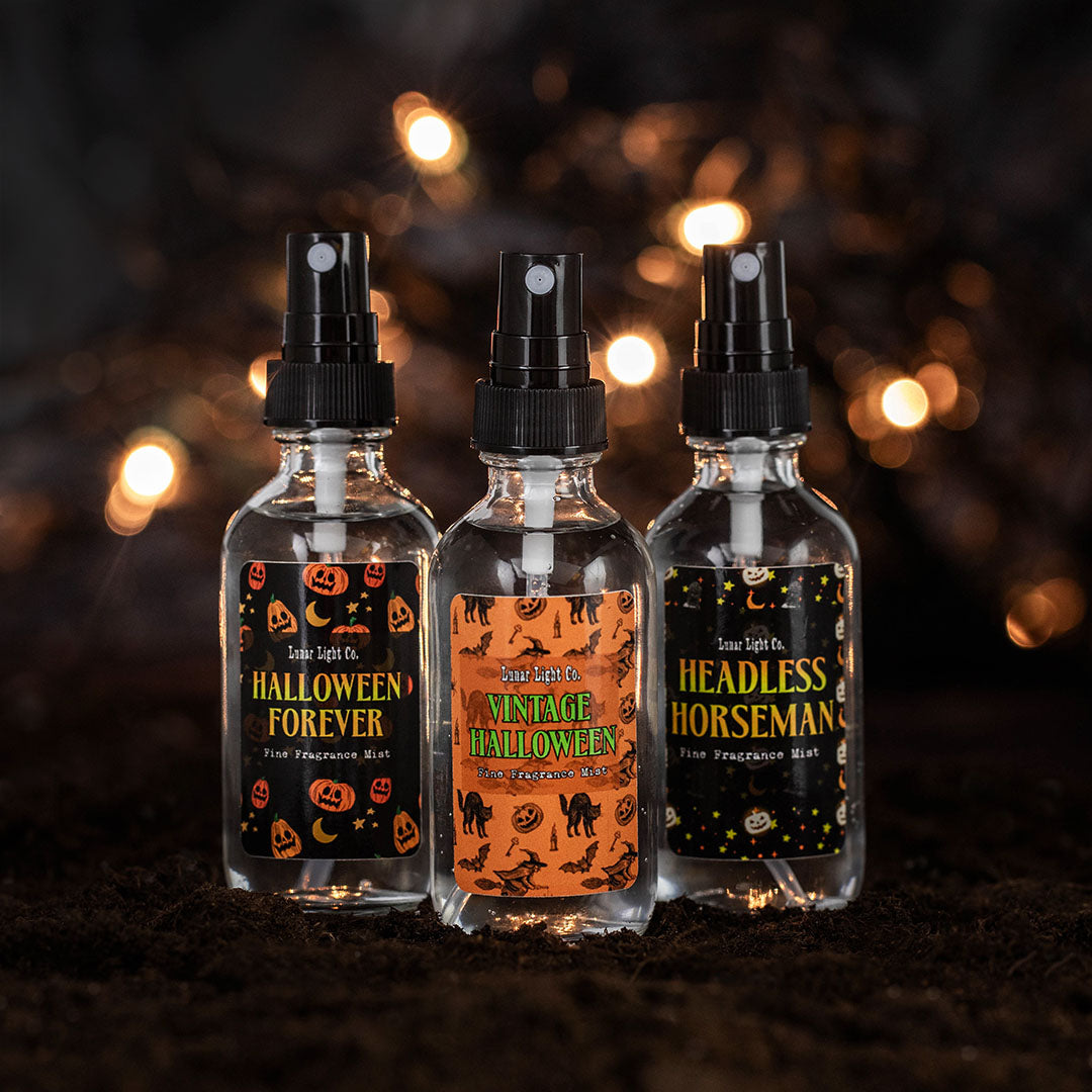 Three glass spray bottles with vintage-halloween inspired labels on dirt with bokeh lights in the foggy, mysterious background