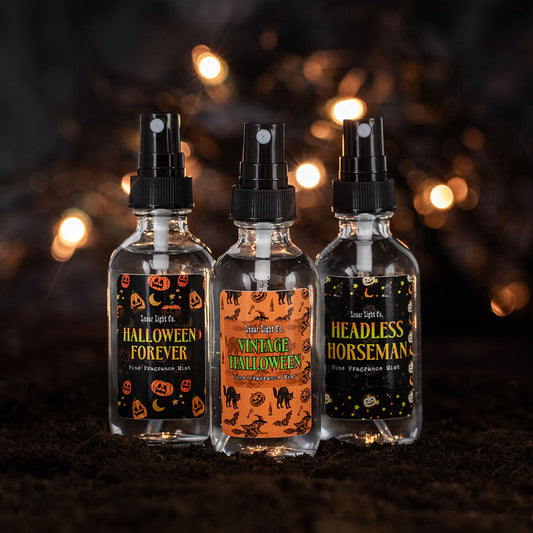 Three glass spray bottles with vintage-halloween inspired labels on dirt with bokeh lights in the foggy, mysterious background