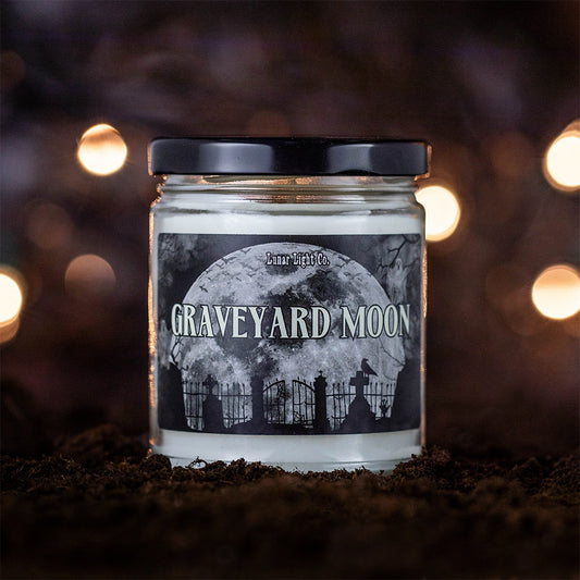 Graveyard Moon candle displayed on dirt with mysterious lights in background