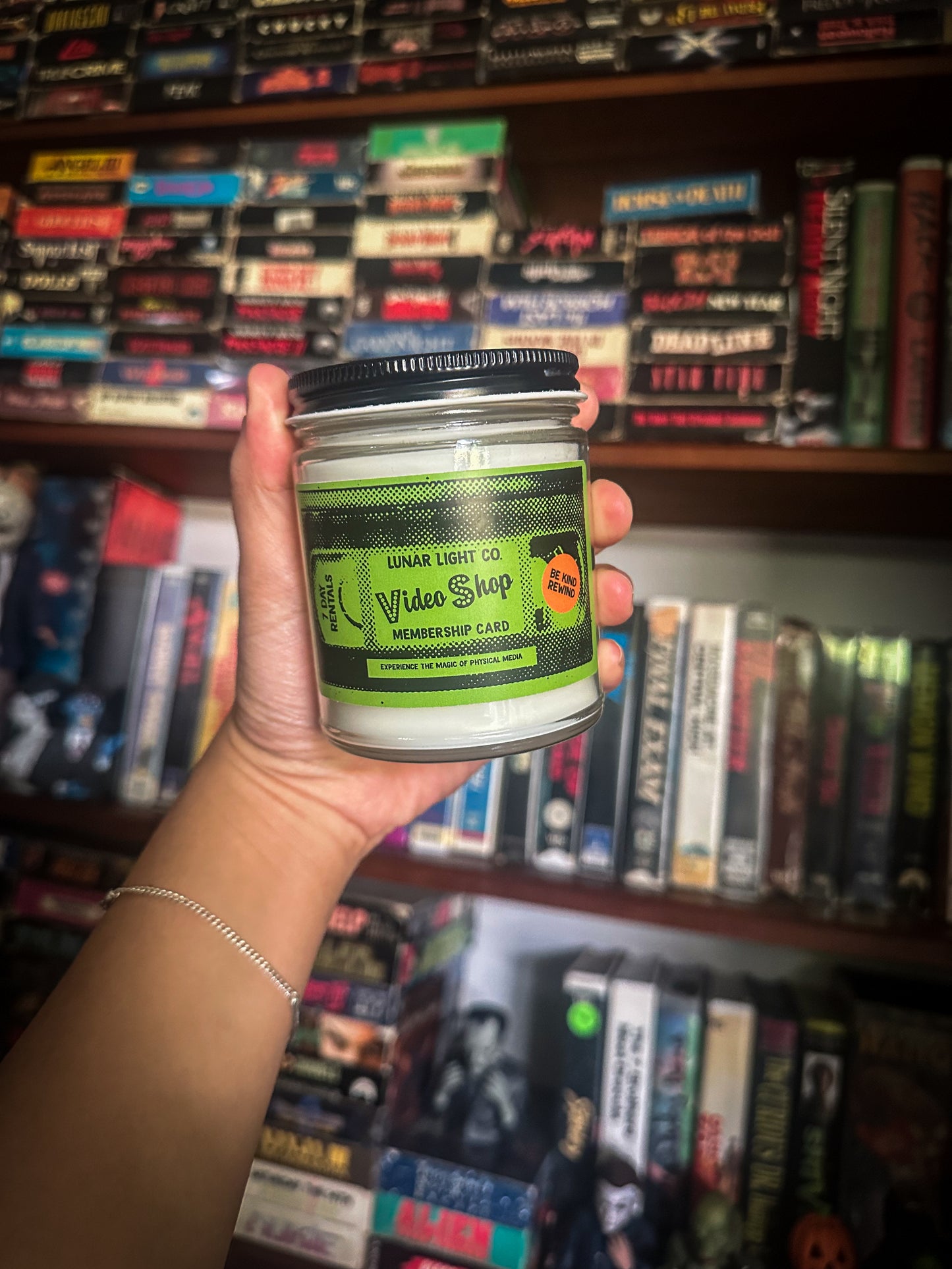 lunar light co movie night candle being held in front of vhs tapes on a shelf